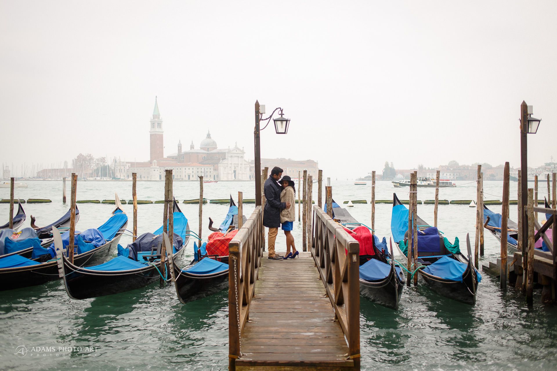 the couple between gondolas on a wooden bridge in Venice