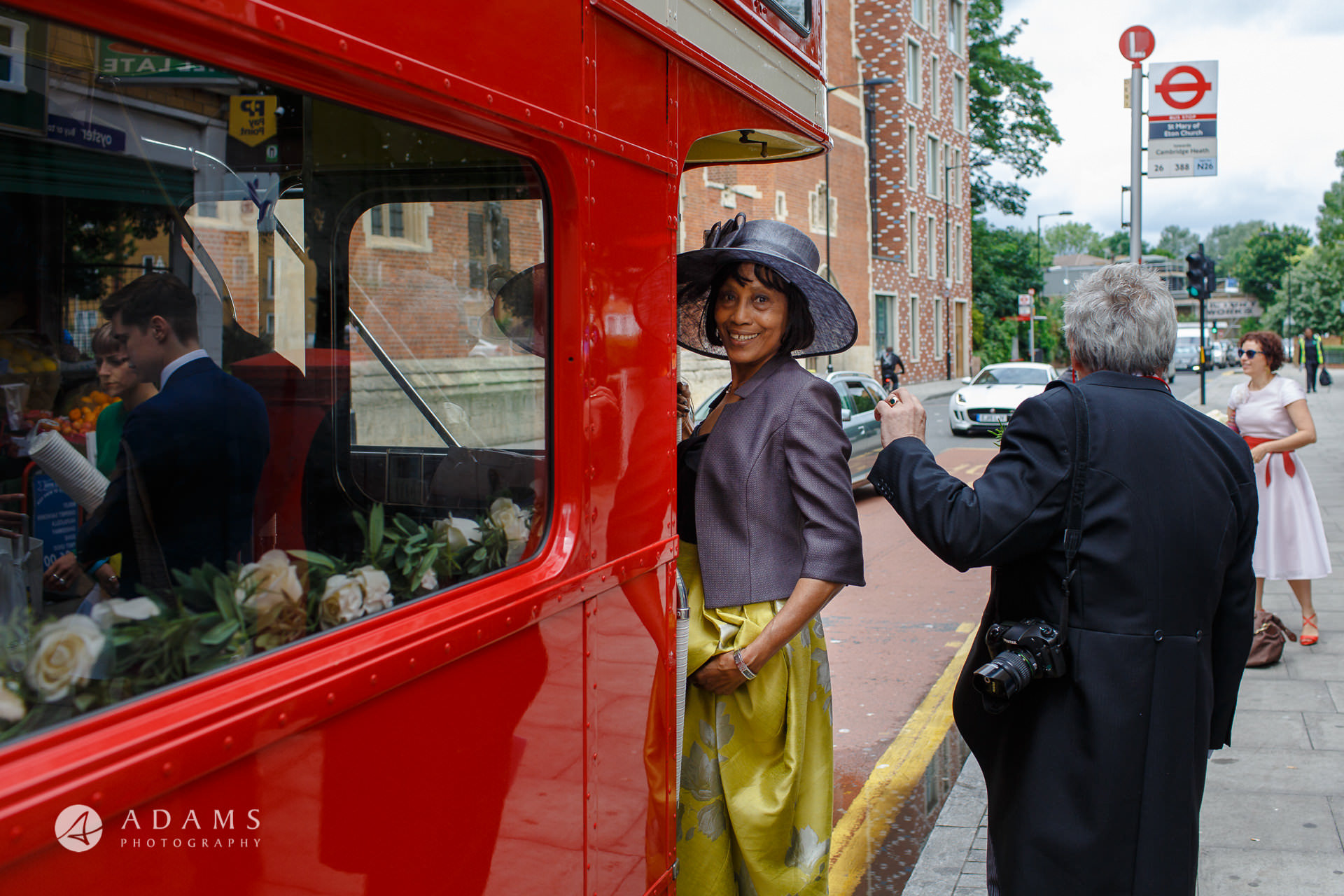 mother of the bride is getting on the red route-master bus in front of the st Mary of Eton church in hackney wick after the wedding ceremony