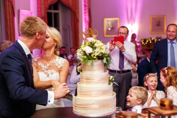 London Wedding Photographer couple cutting the cake and kissing while the kids are playing and laughing in the background