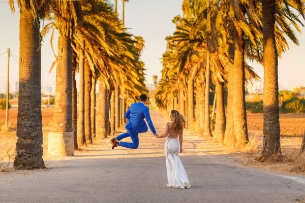 destination wedding photographer couple walks and jumps among the palms
