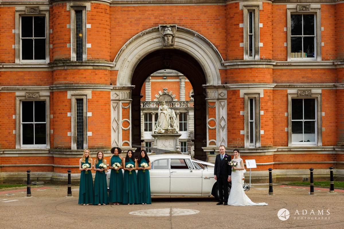 royal holloway wedding photographer bride groom and the bridesmaids posing by the car in front of the university entrance