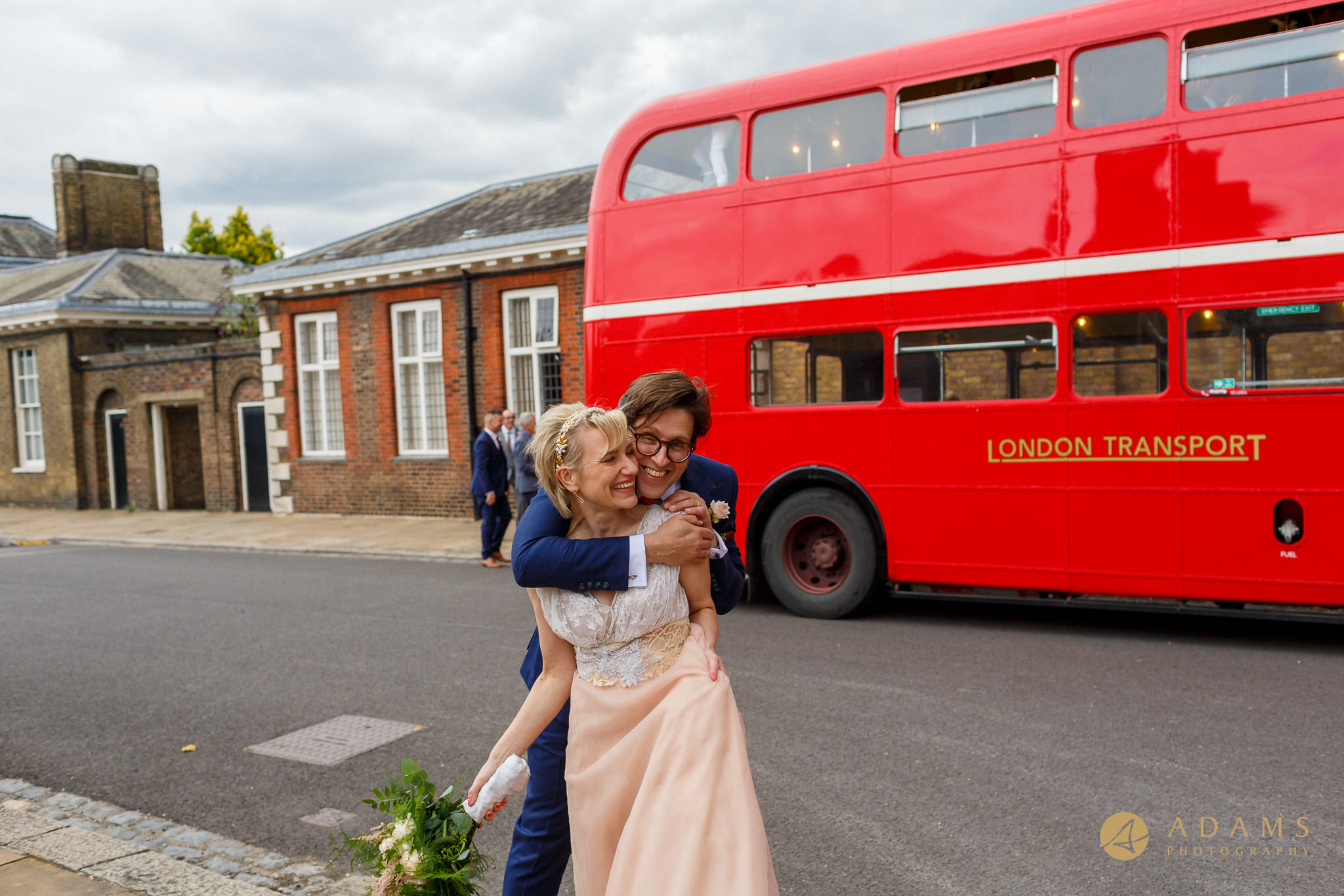 Newlyweds are hugging in front of the red bus