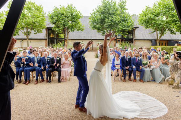 Bury Court Barn Wedding Photo of Bride and Groom raise there hands in happiness