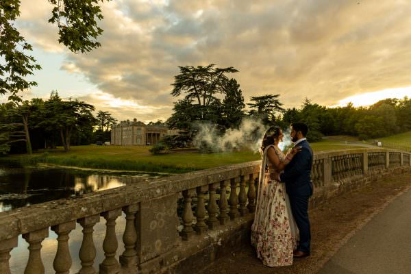 bride and groom posing on the bridge with a view of Compton Verney