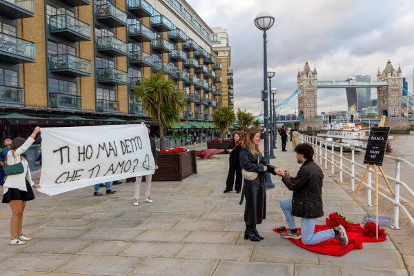 Marriage proposal at Tower Bridge Butlers Wharf with friends involved and holding a sign