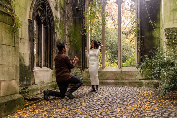 Man on his knee at St Dunstan in the East Church Garden proposing to his fiancé